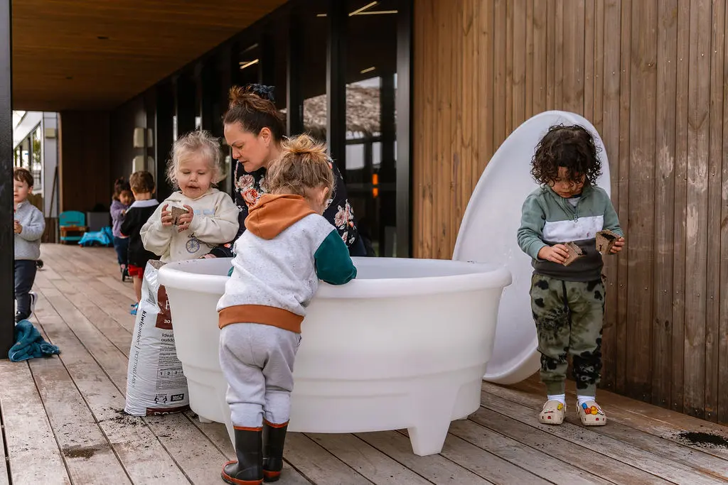 Teacher and toddlers exploring potting mix in a White PlayTray on a centre deck