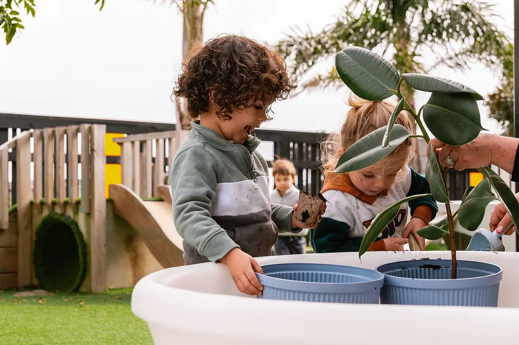 Two preschoolers planting rubber plants in pots inside a White All-in-One PlayTray